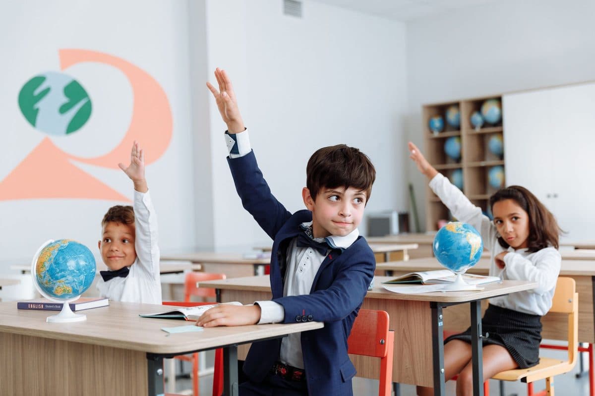 Primary school students at their desks raising their hands to answer a question