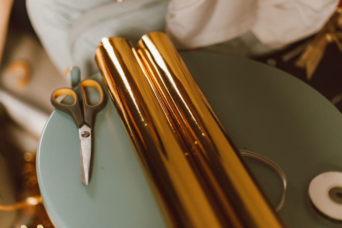 A roll of gold wrapping paper and a pair of scissors on a table, ready for gift wrapping