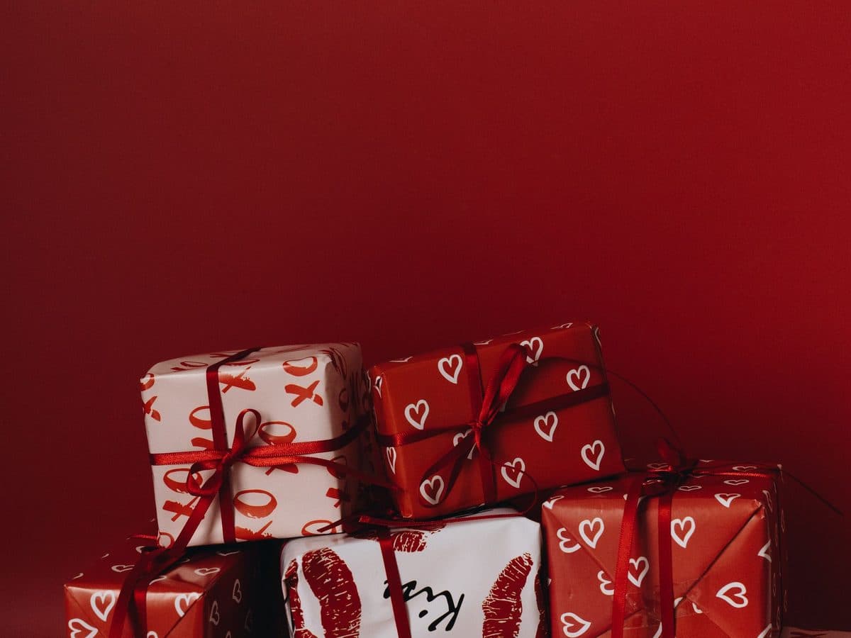 A stack of presents wrapped in red and white paper against a dark red wall
